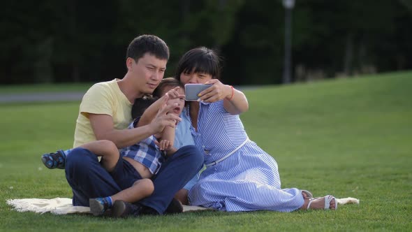 Joyful Asian Family with Kids Taking Selfie in Park