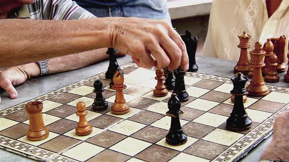 Elderly Men playing Chess and others Watching Outdoors.