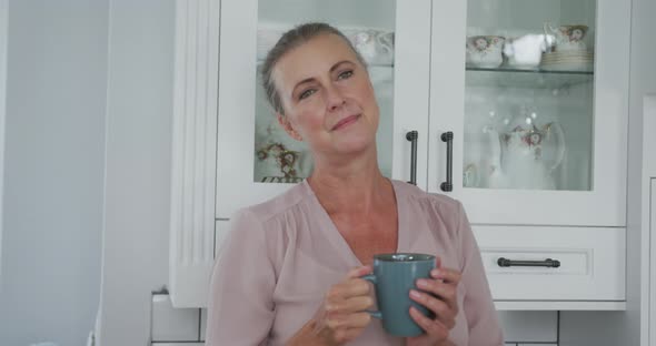 Senior caucasian woman wearing pink shirt and holding mug of coffee in kitchen