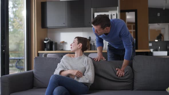 Caucasian Man Talking with Jealous Woman Sitting on Couch in Living Room