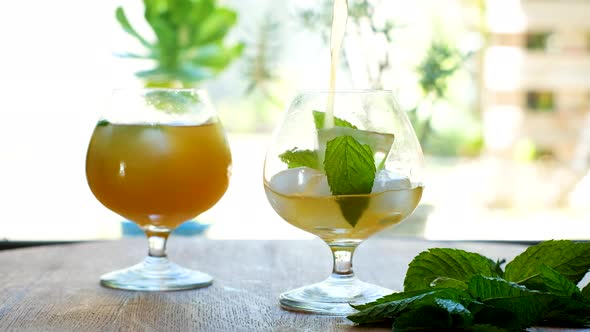 Pouring kombucha into a glass with ice and mint leaves; bright backlit