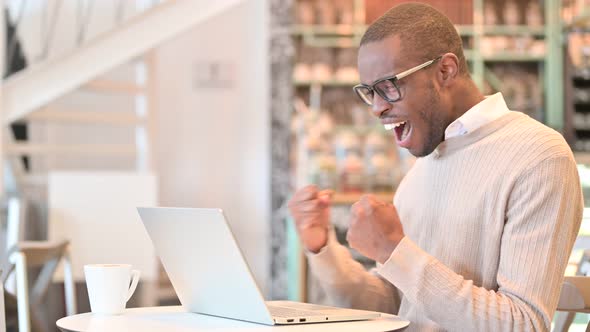 Excited African Man Celebrating Success on Laptop in Cafe