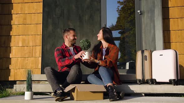 Lovely Modern Young Man and Woman Which Sitting on the Steps, Holding in their Hands Green Flower
