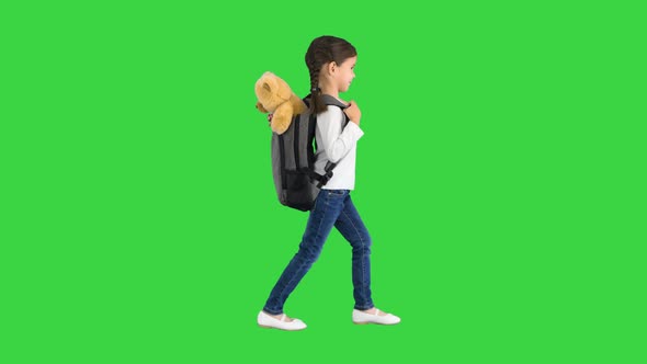 Cute Little Girl Walking To School with a Teddy Bear Sticking Out of Her Backpack on a Green Screen