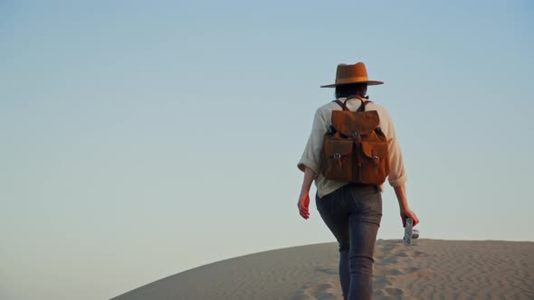 Attractive photographer with a backpack walking on the sand in summer on a clear day