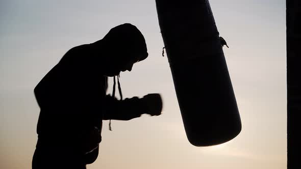 Boxer beats punching bag on sunset background. Silhouette motivation sport boxing. Epic video.