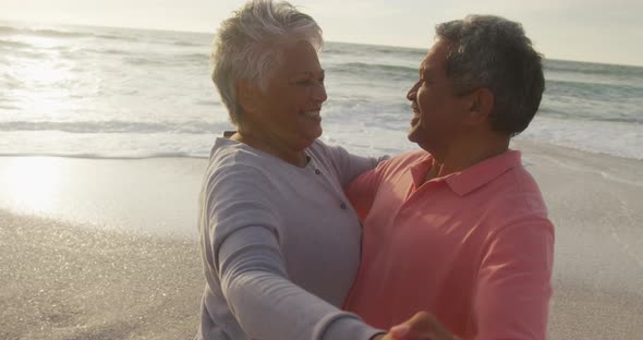 Happy hispanic senior couple dancing on beach at sunset