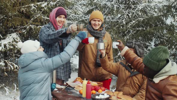 Friends Toasting with Drinks at Campsite in Winter Forest