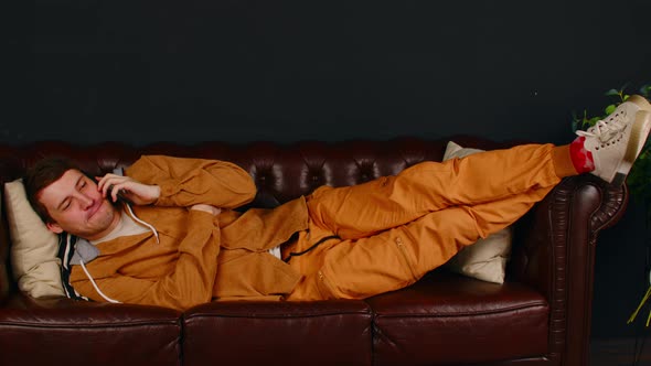 Young man speaks on smartphone, lying on sofa.