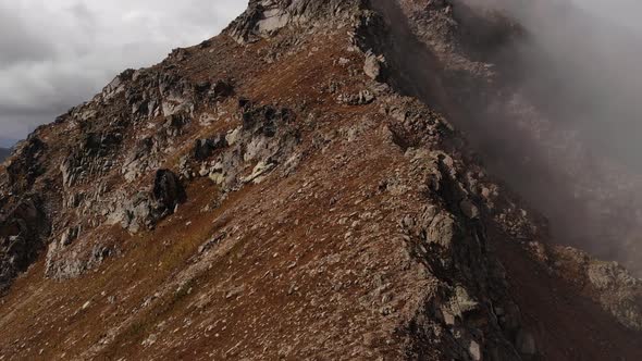 Aerial View of Flight Around a Cliff Top Through Clouds High in the Mountains During the Day