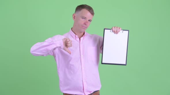 Portrait of Stressed Businessman Showing Clipboard and Giving Thumbs Down