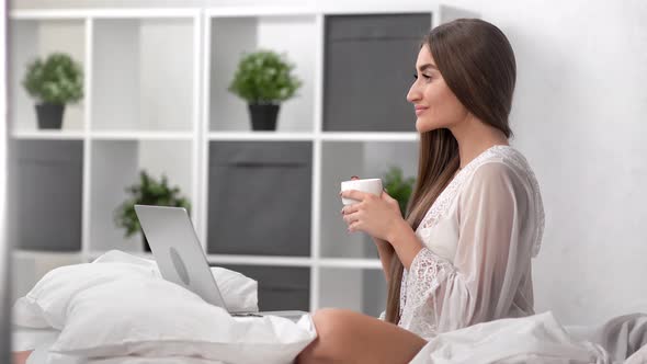 Seductive Girl in Pajamas Drinking Morning Coffee in Front of Laptop