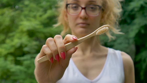 Young Beautiful Girl with Ponytail is Holding a Useful Bamboo Toothbrush and Looking at the Camera