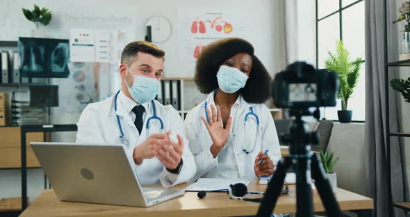 Doctor in Medical Mask Presenting His Female Colleague During Streaming on camera