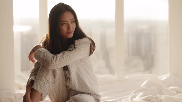 Asian Woman Sitting on a Bed at Home