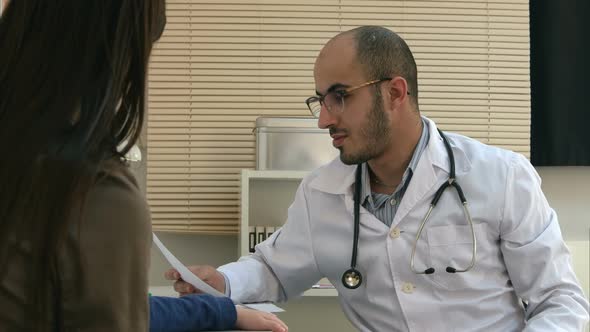 Young Doctor in Glasses Explaining Diagnosis To Mother and Her Child