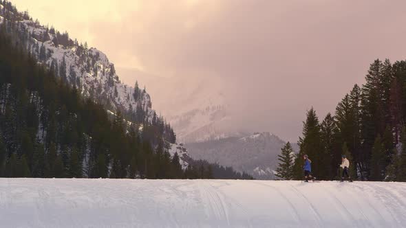 Two women snowshoeing on hilltop with dog at sunset