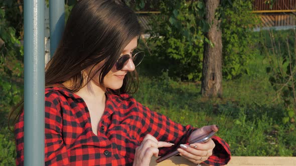 Girl Uses a Mobile Phone in City Park