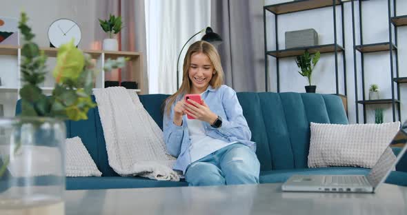 Girl with Long Hair in Casual Clothes Sitting on the Sofa and Revisioning Funny Videos on Mobile