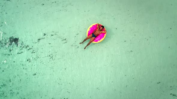 Aerial view of man floating on inflatable donut mattress, relaxing.