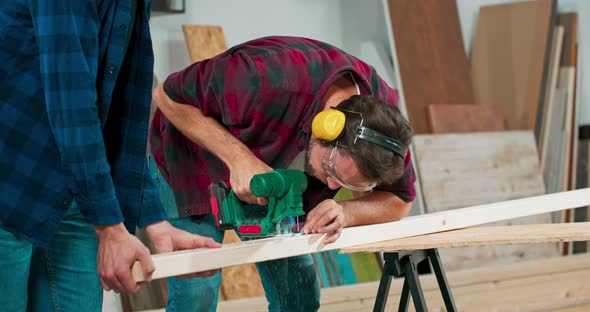 Young Carpenter Cuts an Osb Board with a Jigsaw Craftsman's Hands in Cloth Protective Gloves The