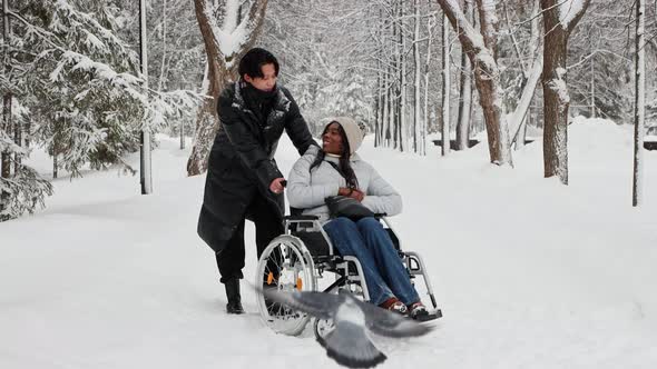 Young Asian Man and His Black Girlfriend in the Wheelchair Talking on the Snowy Path