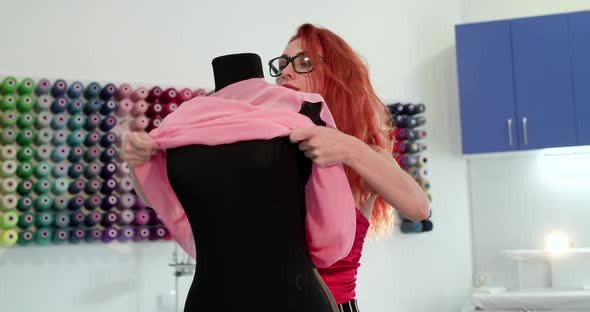 Female Tailor in Glasses Tries the Dress on Mannequin at Mirror and Smiles