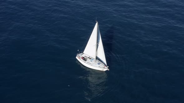 Sail boat sailing slowly towards a setting Sun in the Mediterranean Sea.