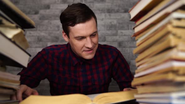 Man Student Boring Reading Book at Library with a Lot of Books in University. Student Disheartened