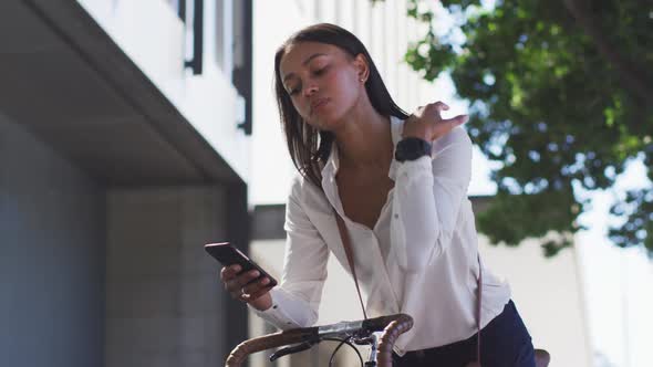 African american woman using smartphone leaning on bike in street