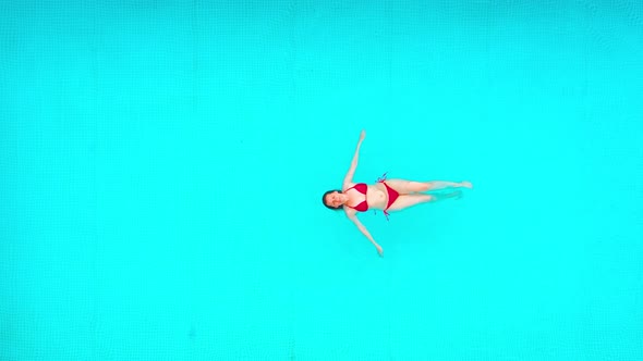 View From the Top As a Woman in Red Swimsuit Swims on Her Back in the Pool