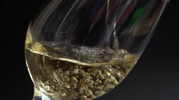 Wine is poured into a glass on a black background. Slow motion.