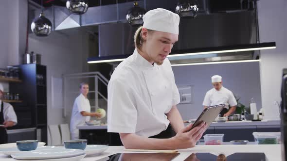 Caucasian male chef wearing chefs whites in a restaurant kitchen using a tablet