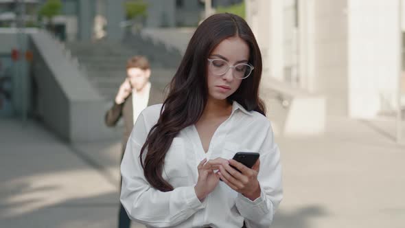 Pretty Business Woman in Eyeglasses Using Smartphone on Street of Business Center Downtown