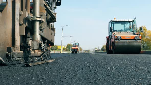 Front View of Bitum Spreaders Riding Along the Road. Constructions Workers Working on Road