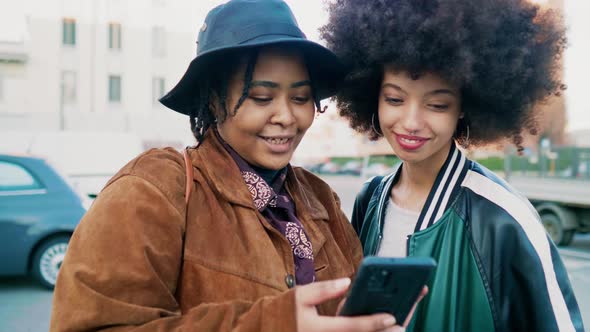 Two women standing in the street looking at messages on smartphone