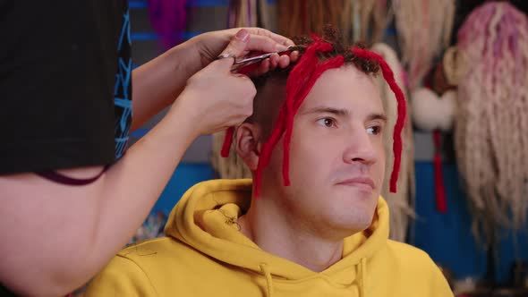 Unrecognizable Person Unwinds Red Dreadlocks for Young Man in Salon