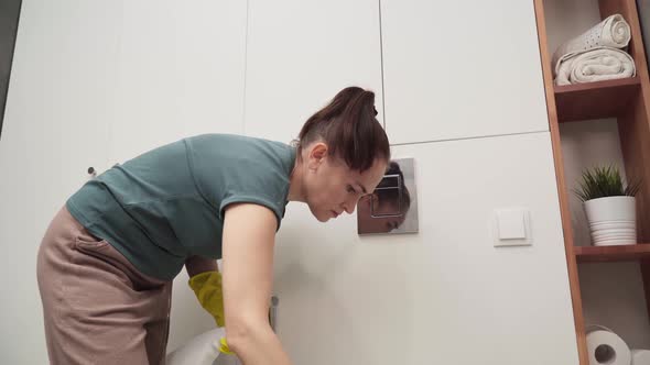 A Woman Wipes a Toilet Bowl in a Bathroom with a Rag