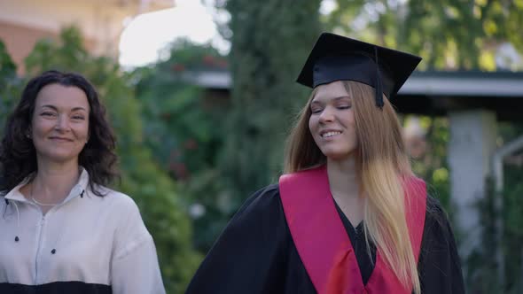 Confident Mature Mother and Grad Daughter Walking in Slow Motion on Front Yard on Graduation Day