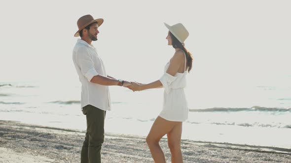 Loving Young Couple in Hats Staring Into Each Other's Eyes and Kissing While Standing Hand in Hand