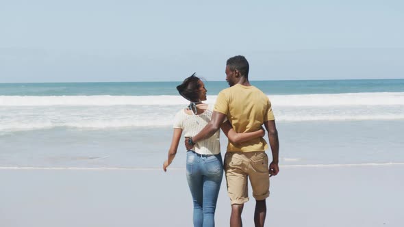 Rear view of african american couple hugging each other and walking at the beach