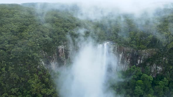 Cinematic view flying through mist clouds to reveal a majestic waterfall flowing into a tropical rai