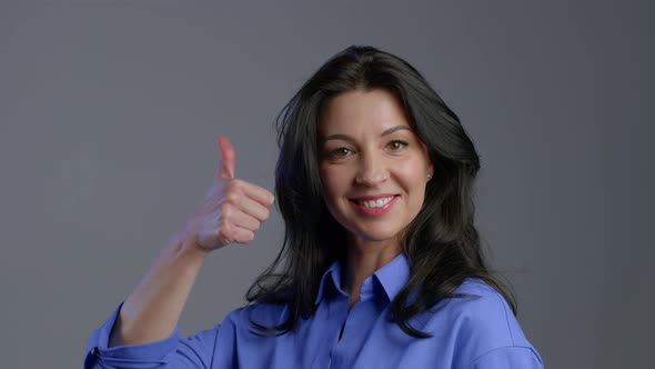 Happy Adult Woman on Grey. Lady with Long Hair in Blue Shirt Shows Yes Like