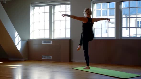 a Barefoot Woman Is Dressed in Black Athletic Clothing and Stands on a Gym Mat. She Spreads Her Arms