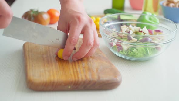 Male Hands are Cutting Small Yellow Cherry Tomatoes on a Cutting Board