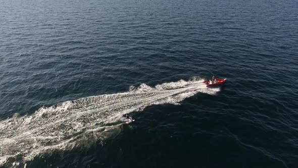 Flyover Drone Footage of Red Inflatable Boat Pulling Male on Board in Sea in Slowmotion