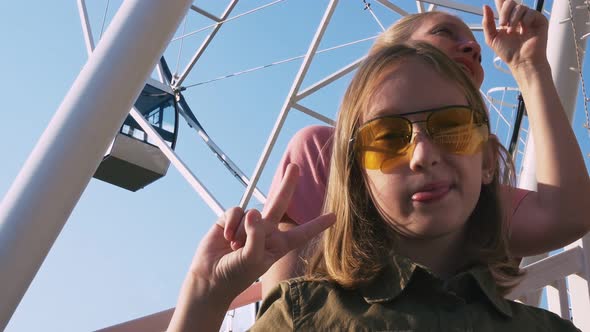 A Teenage Girl in Line on the Ferris Wheel Shows the Language and the Sign of Peace