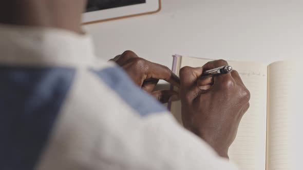 Black Man Writing in Notebook at Dark Office