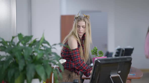 Middle Shot of Concentrated Young Millennial Woman Unpacking at New Workplace As Blurred Woman