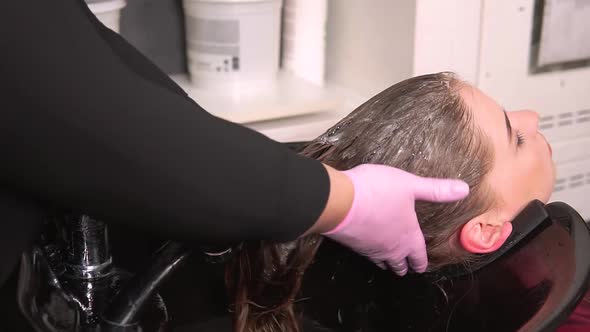 The Hairdresser Uses Massage Movements to Apply Shampoo to the Hair of a Woman